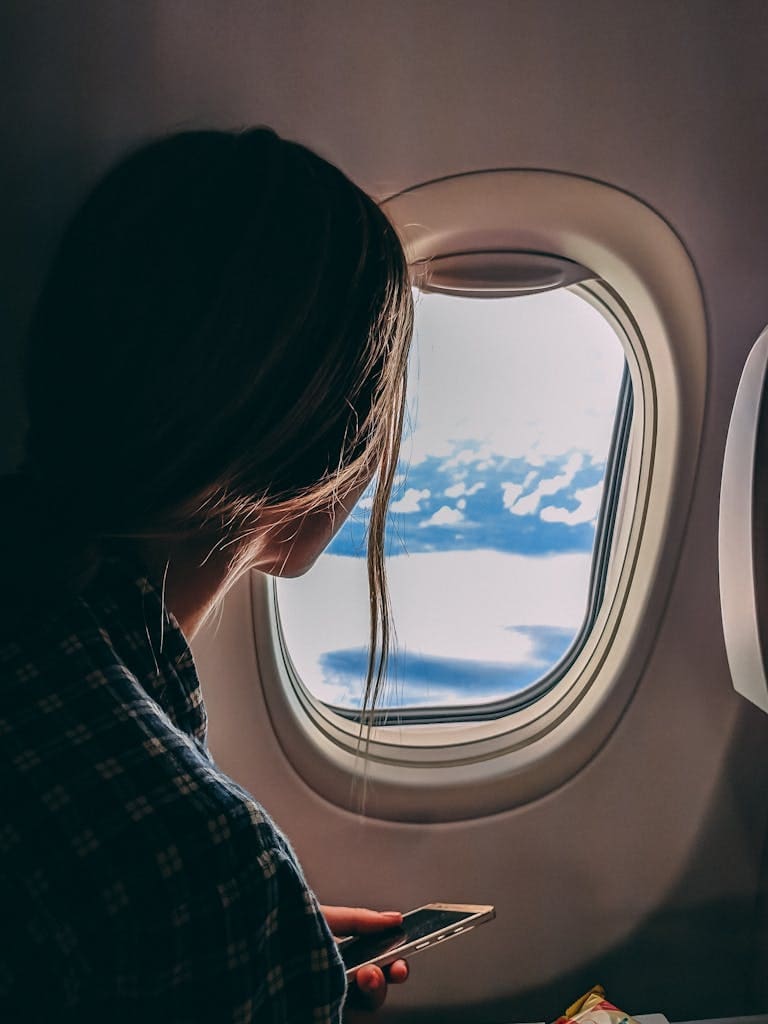 Top Tips When Searching for Cheap Flights | Imagine Greece Retreats A woman looks out an airplane window, capturing a serene view of clouds and sky during a flight.