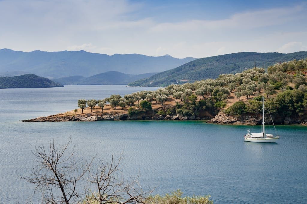Nature Retreat Venue in Evia, Greece | Quiet & Authentic Retreats | Imagine Greece Retreats Tranquil bay view in Greece featuring a lone yacht and serene island landscape.